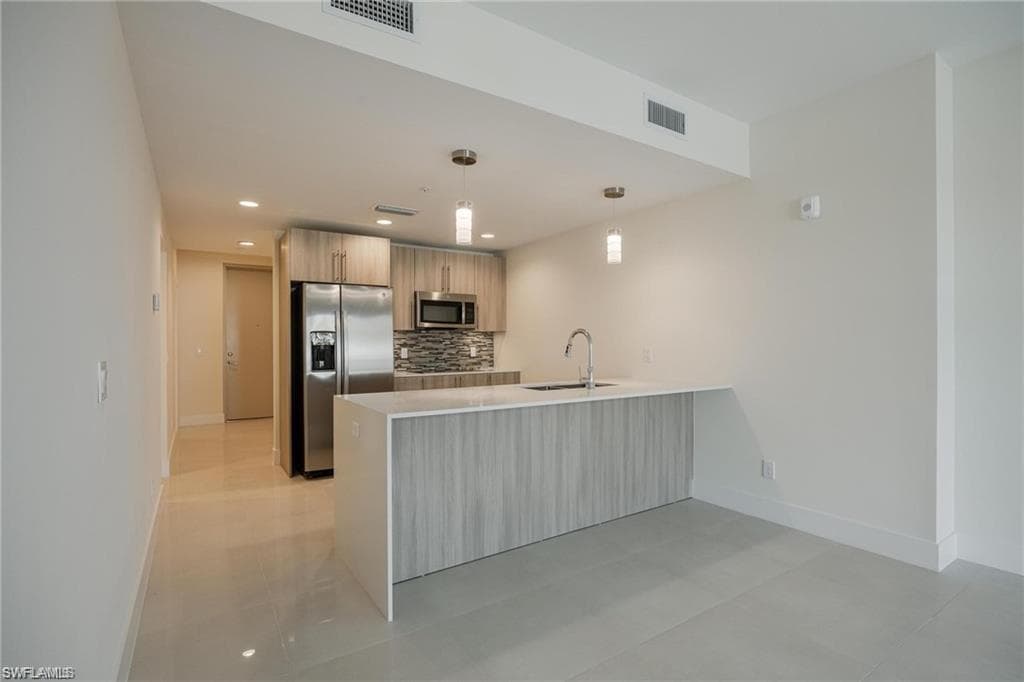 Kitchen with a peninsula, stainless steel appliances, visible vents, and baseboards