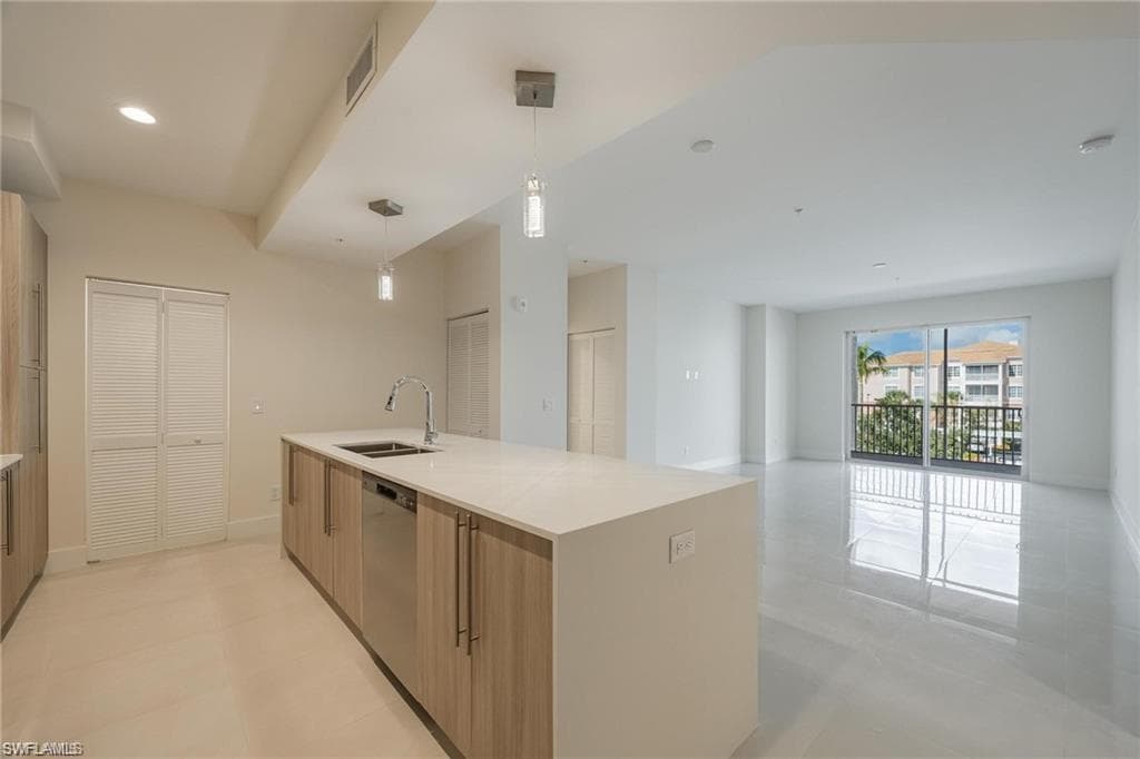 Kitchen featuring light countertops, a sink, open floor plan, dishwasher, and decorative light fixtures