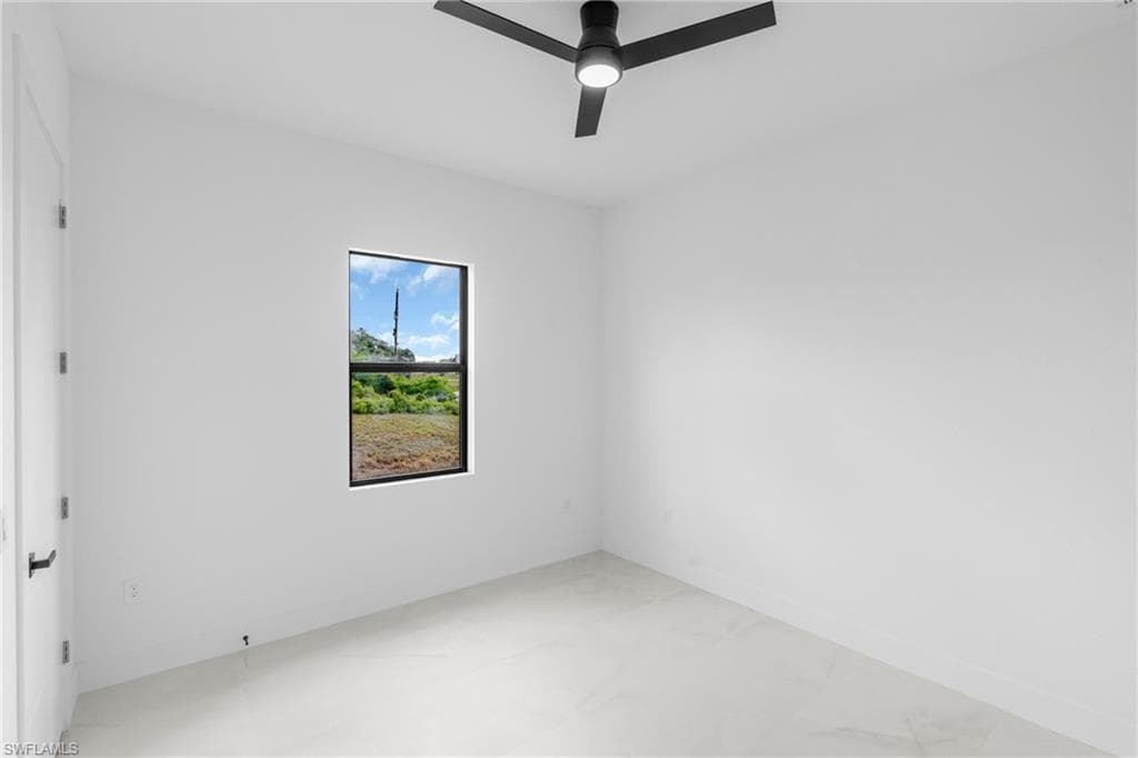 Bright interior space featuring a window with a natural landscape, a contemporary ceiling fan with integrated lighting, a white painted door with a black lever handle, and light-toned tile flooring