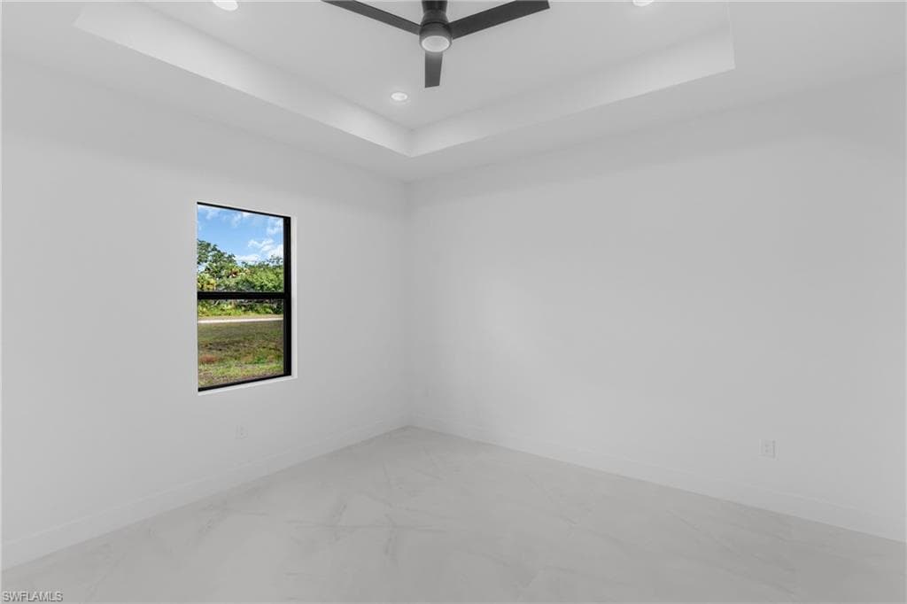 Spacious room featuring a tray ceiling with recessed lighting, a contemporary ceiling fan, a large window with black trim, and light-toned tile flooring