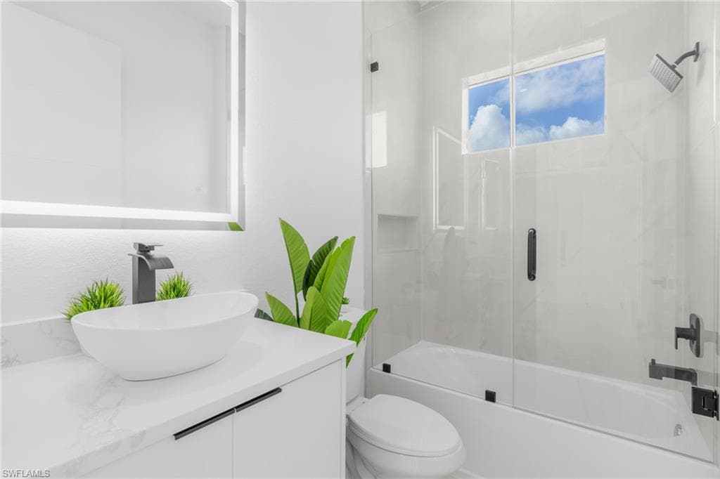 Contemporary bathroom featuring an illuminated vanity mirror, a vessel sink with a matte black faucet, a white countertop, and a glass-enclosed shower over a bathtub with matte black fixtures