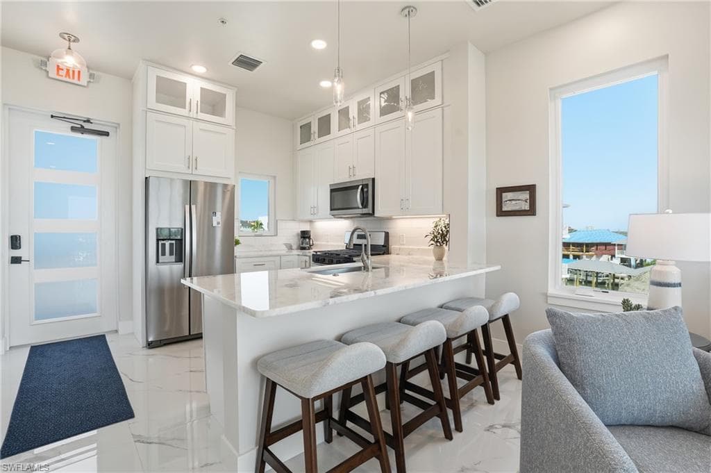 Kitchen featuring stainless steel appliances, white cabinets, a breakfast bar, light stone counters, and a peninsula - Virtually Edited Image