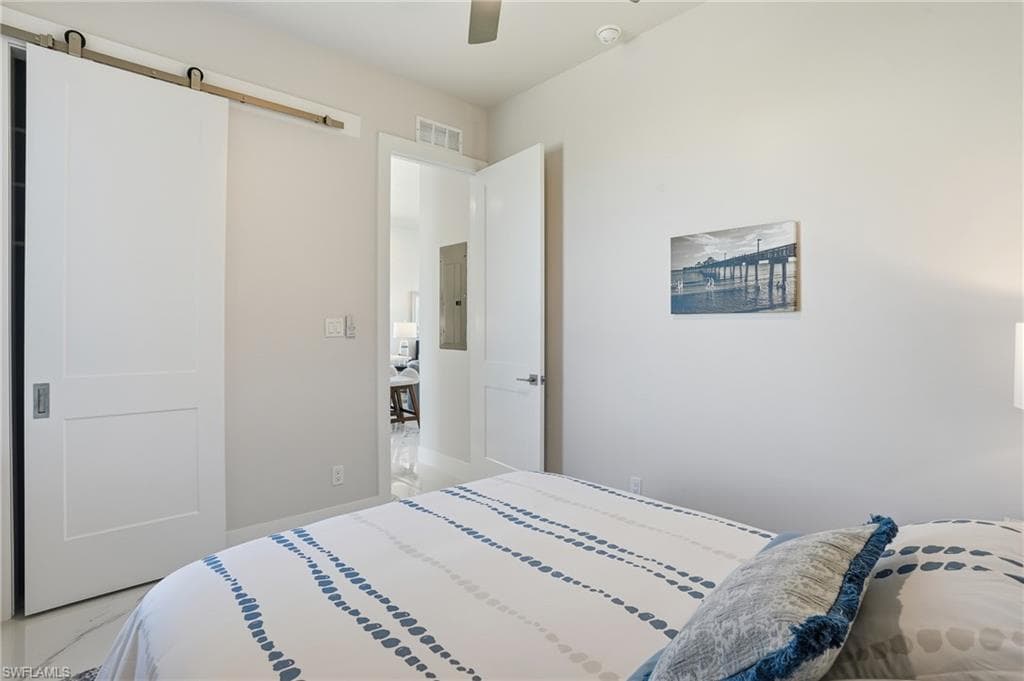 Bedroom featuring a barn door, ceiling fan, and electric panel - Virtually Edited Image