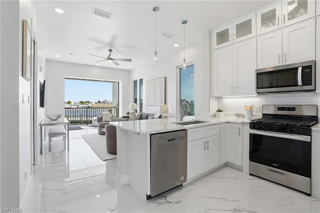 Kitchen with appliances with stainless steel finishes, light marble finish floors, tasteful backsplash, white cabinets, and pendant lighting - Virtually Edited Image