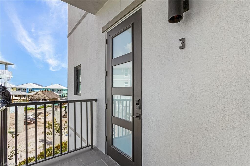 Contemporary entry door with frosted glass panels and sleek black hardware, opening onto a private balcony with black metal railings - Virtually Edited Image