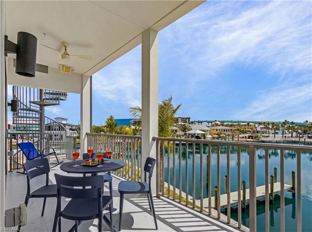 Covered balcony featuring a ceiling fan, spiral staircase, and marine railing overlooking a waterway with boat slips - Virtually Edited Image