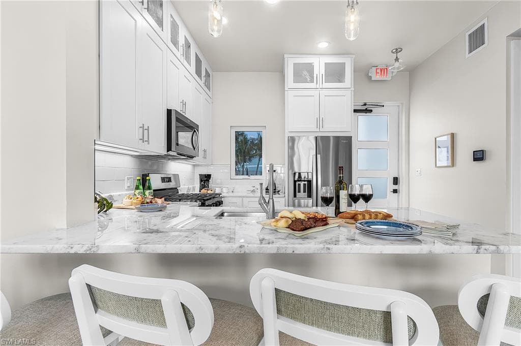 Kitchen featuring white shaker cabinetry, stainless steel appliances, a white subway tile backsplash, and a large island with a light-toned, veined countertop - Virtually Edited Image