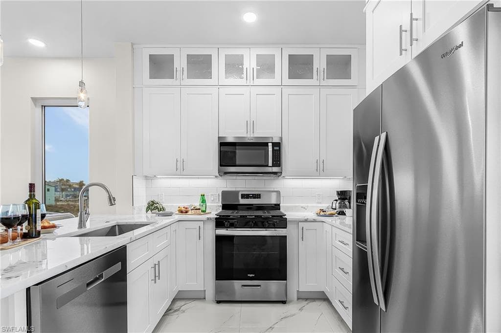 Modern kitchen featuring white shaker cabinetry, stainless steel appliances, marble-look countertops, a subway tile backsplash, and recessed lighting - Virtually Edited Image