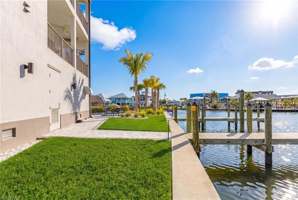 Waterfront property featuring a private boat dock, manicured lawn, and mature palm trees - Virtually Edited Image