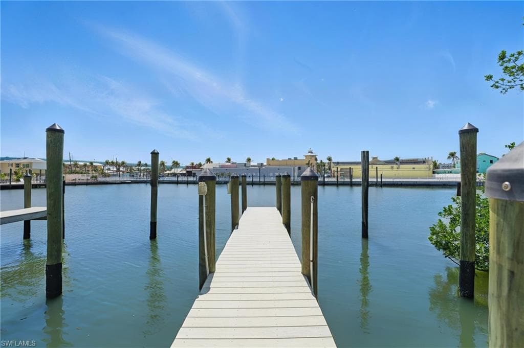 Waterfront dock with white decking extending into calm water, featuring multiple mooring pilings - Virtually Edited Image