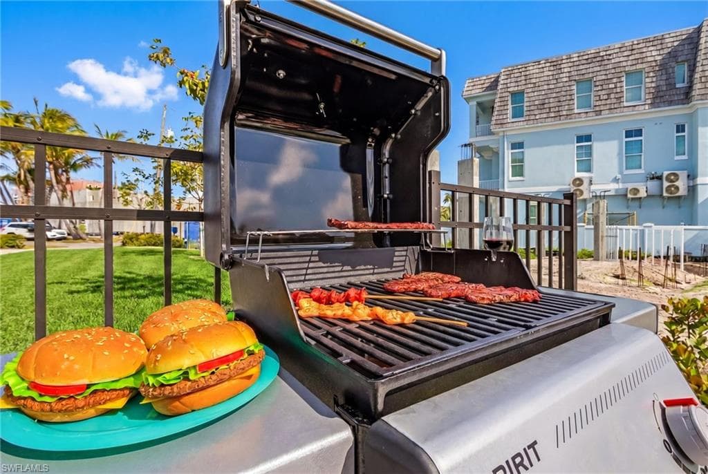 Outdoor grill area with a black metal fence and partial views of a multi-story structure with a gambrel roof and light blue siding - Virtually Edited Image