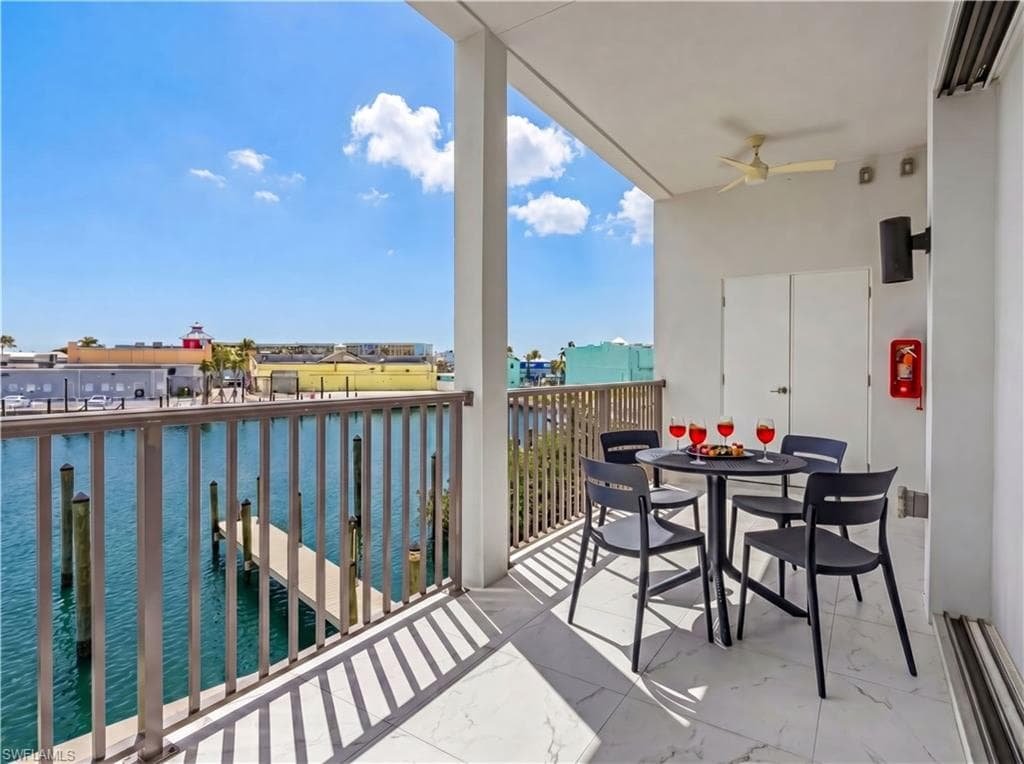 Waterfront balcony featuring a white marble-look tile floor, a metal railing, a ceiling fan, and built-in outdoor lighting - Virtually Edited Image