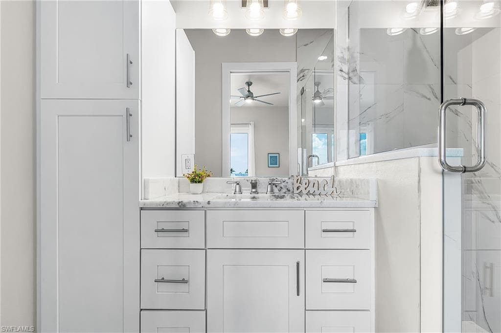 White shaker-style cabinetry with brushed nickel hardware, a single vanity with a white countertop, an undermount sink with a chrome faucet, and a large mirror with overhead lighting - Virtually Edited Image