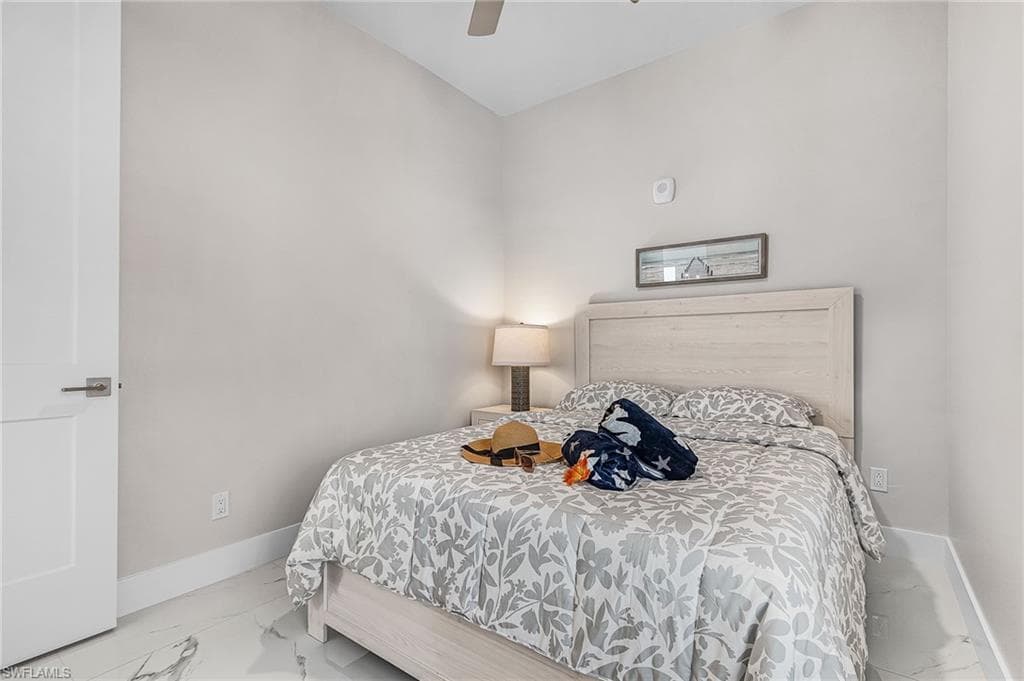 Spacious bedroom featuring light neutral wall tones, a modern ceiling fan, and white baseboards - Virtually Edited Image
