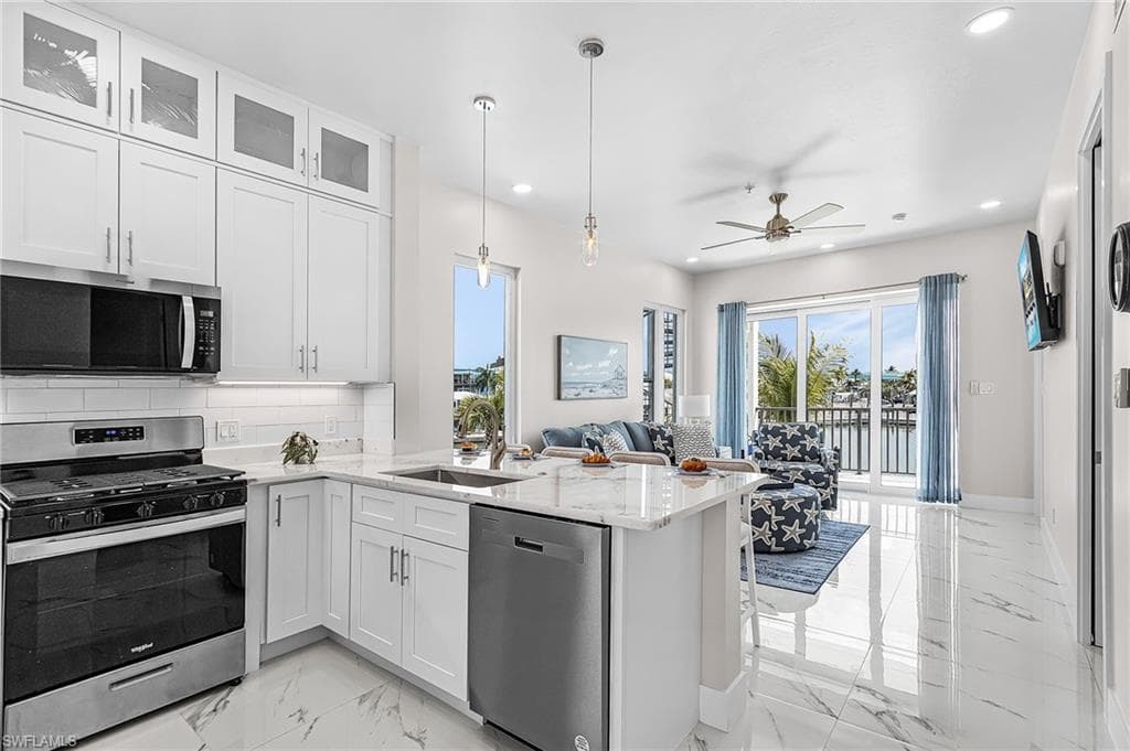 Open-concept living space with white kitchen cabinetry, stainless steel appliances, and a central island with a sink - Virtually Edited Image