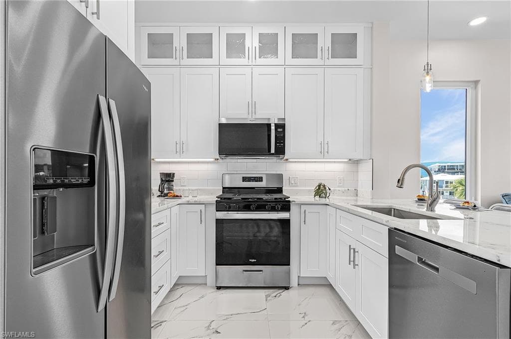 Contemporary kitchen featuring white cabinetry, stainless steel appliances, and white marble-look flooring - Virtually Edited Image