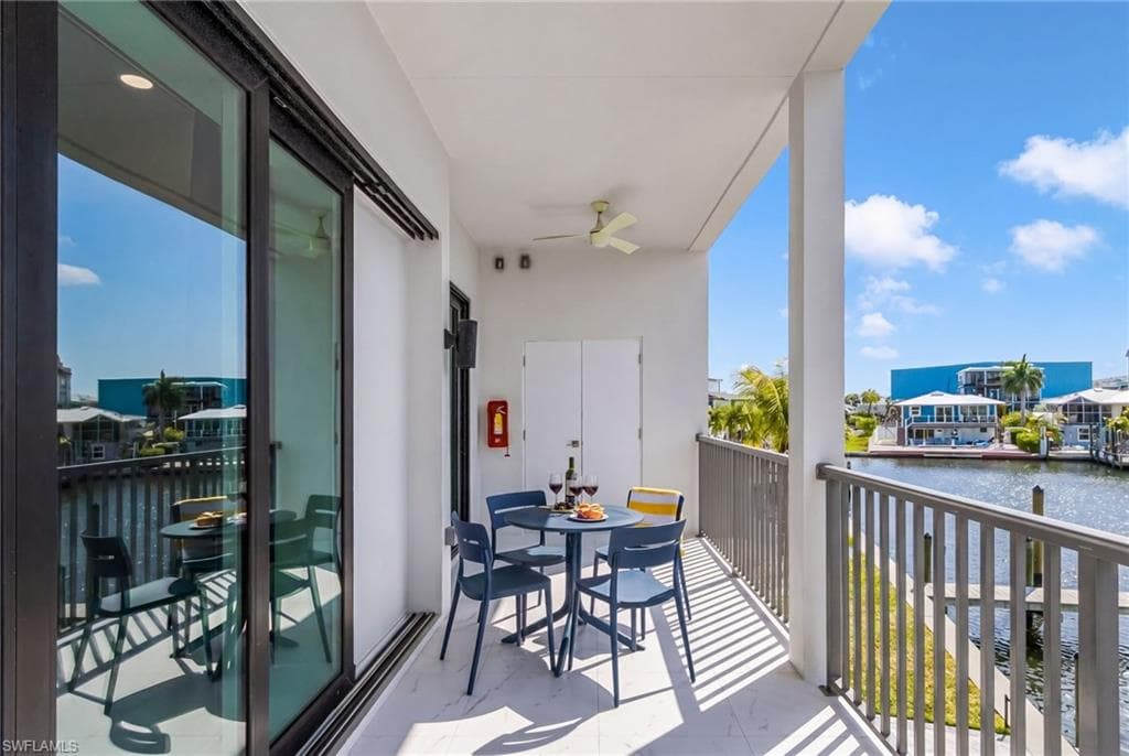 Balcony featuring waterside views, a ceiling fan, sliding glass doors, and a neutral palette - Virtually Edited Image