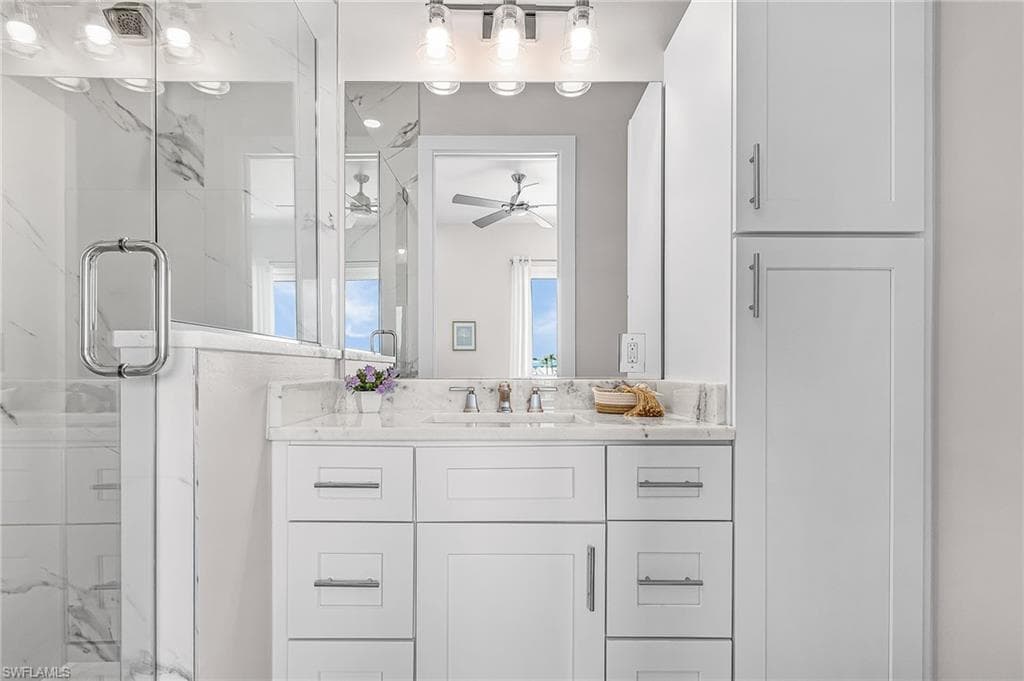Bathroom featuring a single vanity with a white countertop and undermount sink, shaker-style cabinetry with chrome hardware, and a glass-enclosed shower with tile surround - Virtually Edited Image