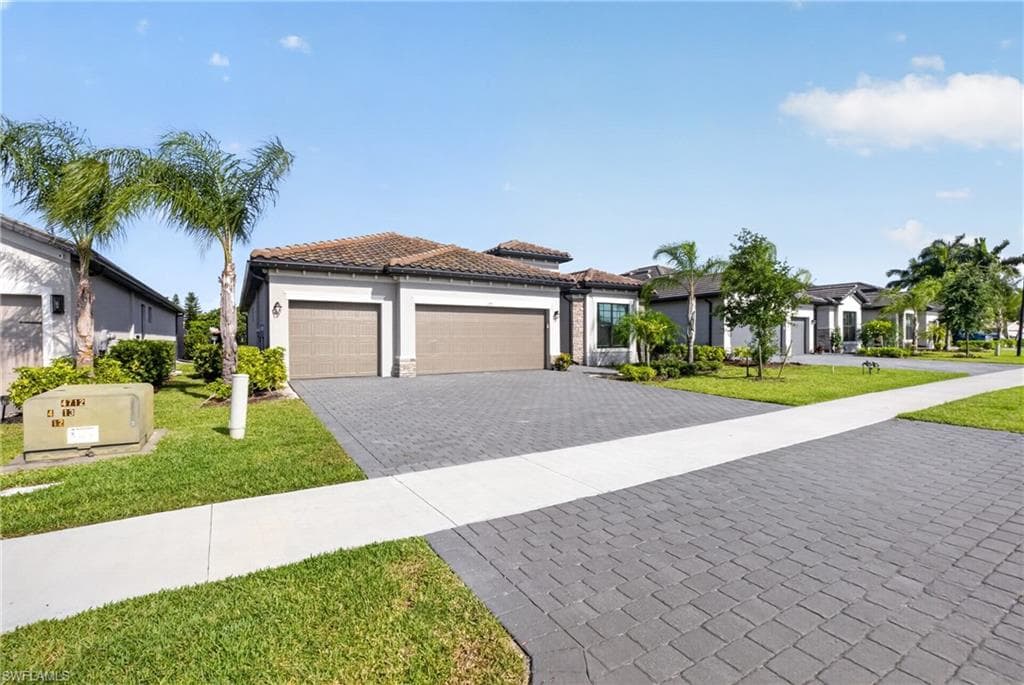 Contemporary stucco exterior with a tile roof, dual garage doors, paver driveway, and mature palm trees