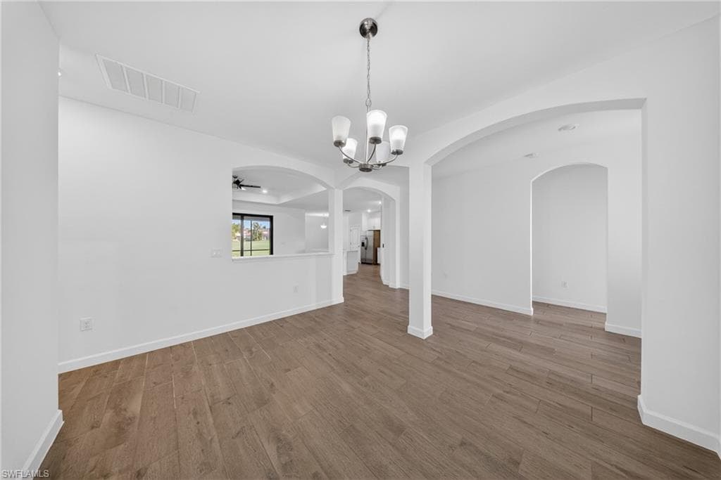 Expansive room featuring wood-finish flooring, a contemporary chandelier, and multiple arched doorways