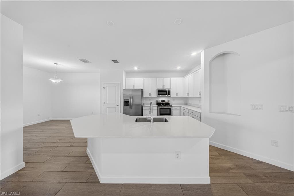 Open-concept kitchen featuring an expansive island with a stainless steel sink, white cabinetry, integrated stainless steel appliances, and recessed lighting