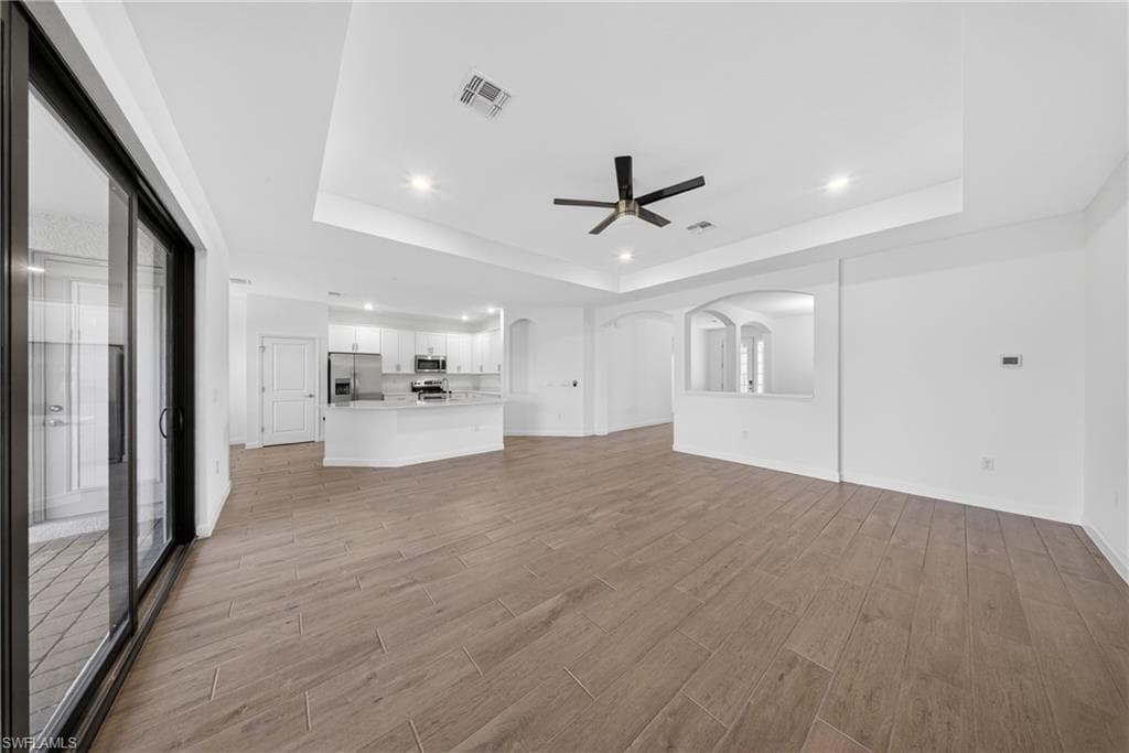 Spacious living area featuring wood-finish tile flooring, a tray ceiling with recessed lighting, and a contemporary ceiling fan