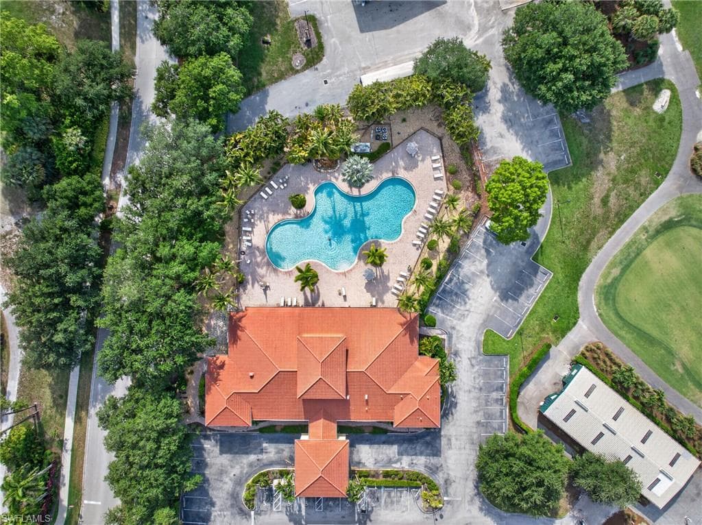 Spanish tile-roofed building featuring a large freeform swimming pool, surrounding lounge areas, mature palm trees, and adjacent paved parking