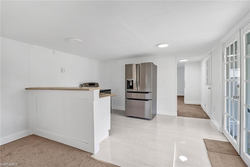 Kitchen with stainless steel fridge with ice dispenser, light colored carpet, a peninsula, white cabinets, and range with electric stovetop