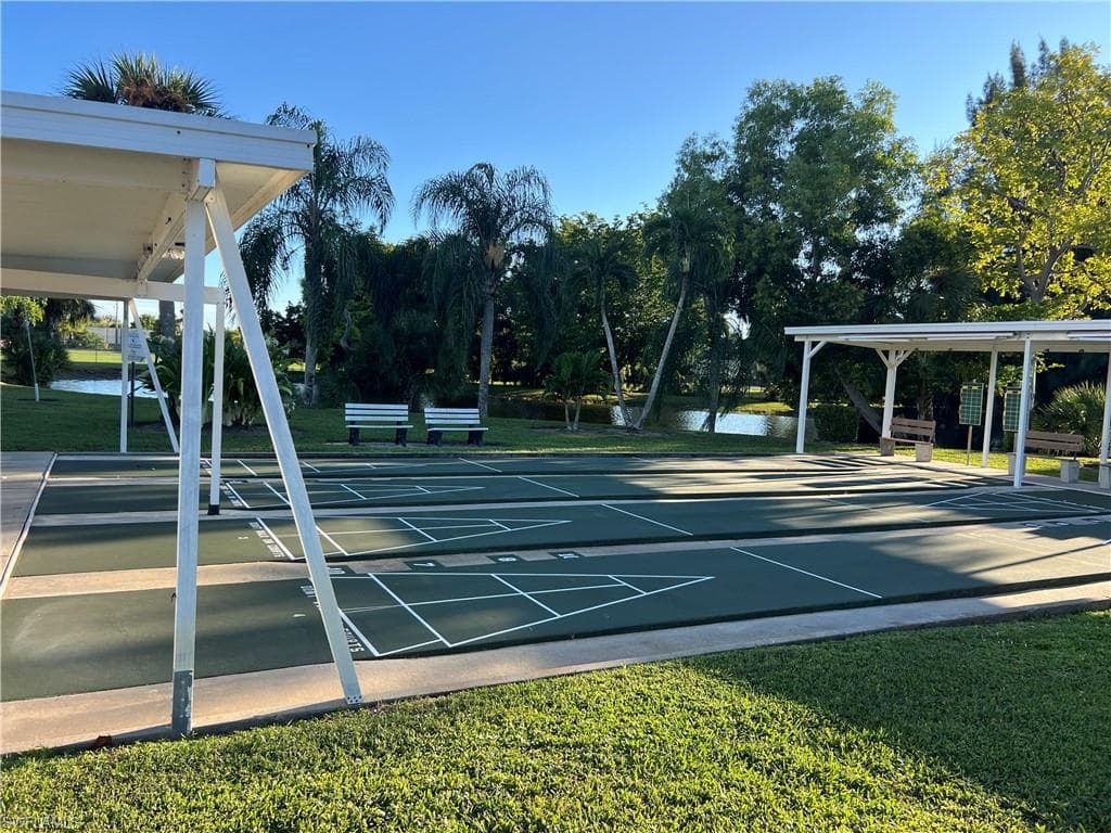 View of home's community featuring shuffleboard, a lawn, and view of wooded area