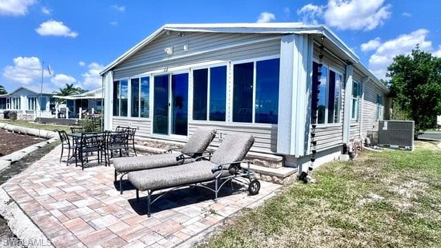 Exterior featuring light-colored siding, a sunroom with large windows, and a paver patio