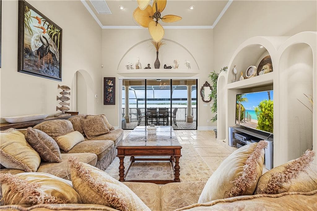 Vaulted ceiling great room featuring stone tile flooring, a decorative ceiling fan, built-in shelving, and direct access to a screened patio overlooking a body of water