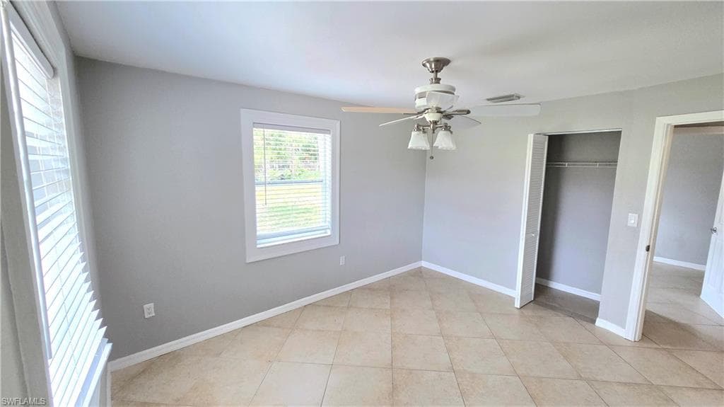 Bedroom #3 featuring light gray walls, tile flooring, a window with horizontal blinds, a ceiling fan with integrated lighting, and an open closet with shelving