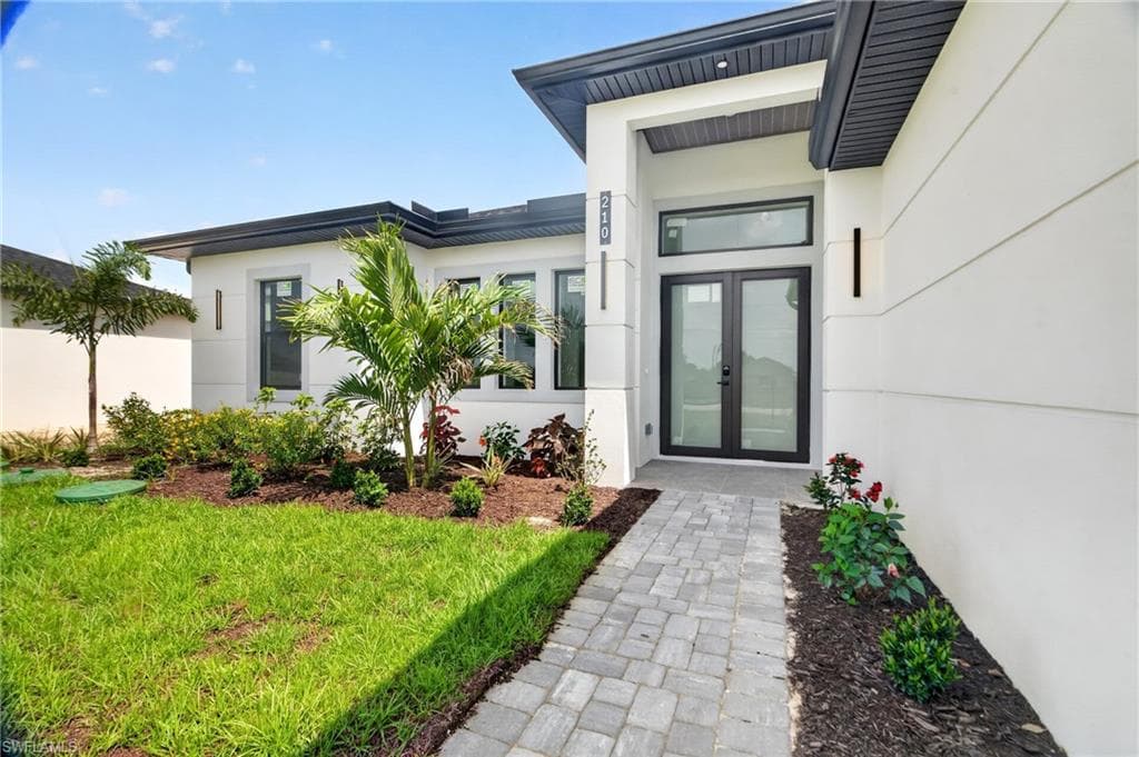 Modern exterior featuring a prominent double-door entry with transom window, contemporary wall sconces, and a paver walkway
