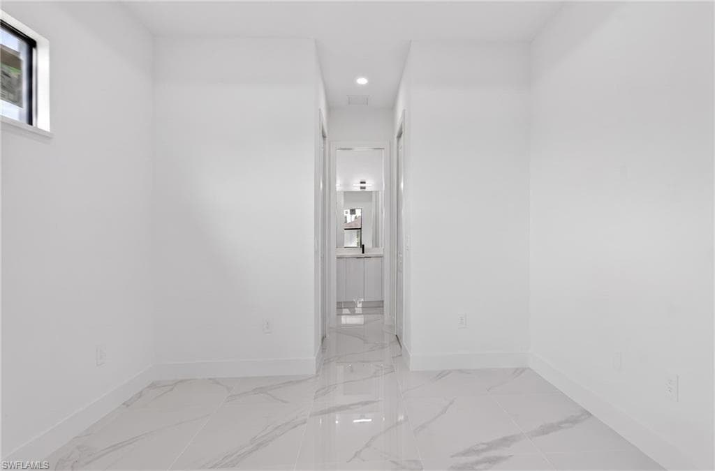 Spacious interior room with white walls, baseboards, and large format marble-look tile flooring