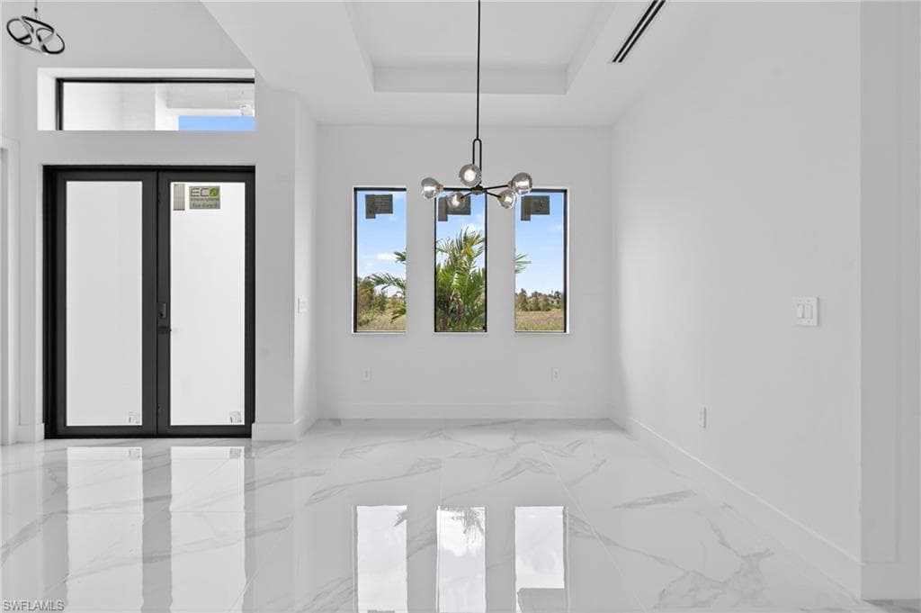 Bright interior space featuring polished tile flooring with veining, a modern linear chandelier, and a tray ceiling