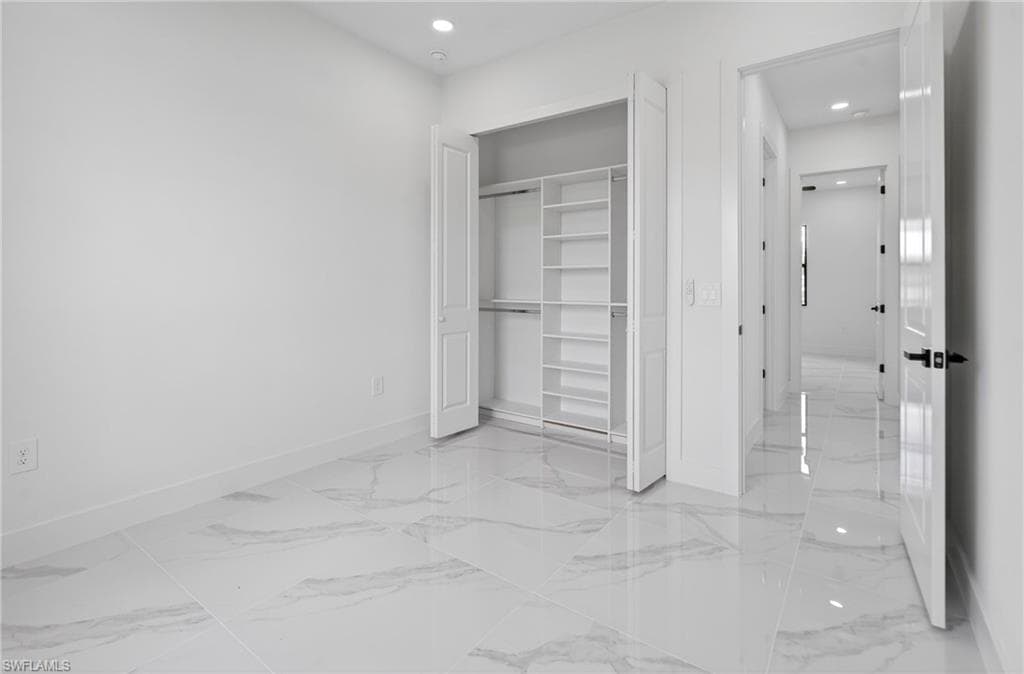 Interior room featuring large format tile flooring, a built-in closet with shelving and hanging rods, recessed ceiling lighting, and a white paneled door with black hardware