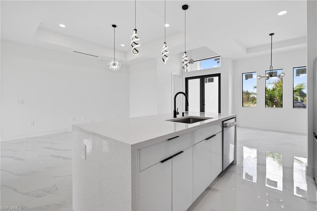 Open-concept space featuring a white quartz-finish island with an undermount sink and matte black faucet, modern white cabinetry with matte black hardware, and an integrated dishwasher