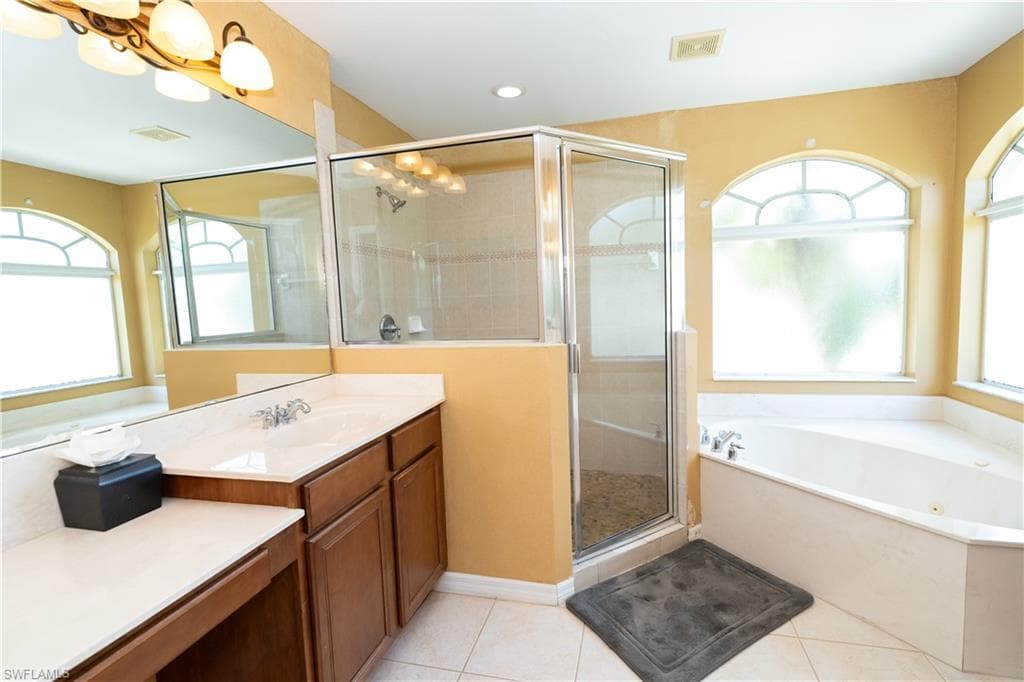 Bathroom featuring a corner soaking tub, a separate glass-enclosed shower, a double vanity with an integrated sink, and arched windows