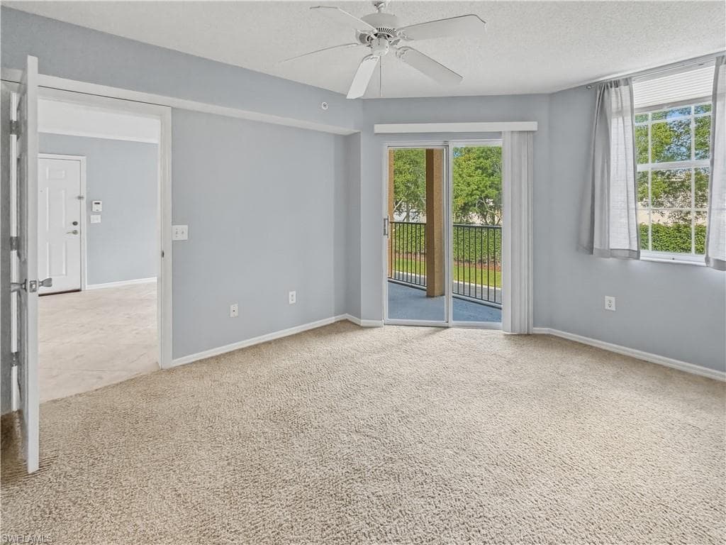 Bright room featuring light blue walls, neutral carpet flooring, a ceiling fan, and a sliding glass door leading to an outdoor balcony