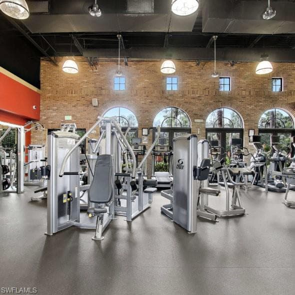 Fitness center featuring ample natural light, arched windows, exposed brick accent walls, high ceilings, and diverse exercise equipment is located steps away from the condo unit.