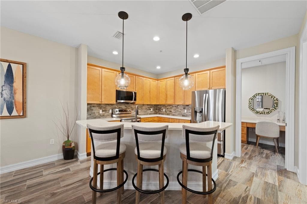Kitchen featuring wood-finish cabinetry, stainless steel appliances, a tile backsplash, and a breakfast bar with pendant lighting. NEW KITCHEN LG-IQ APPLIANCES (2024), NEW QUARTZ COUNTERS (2018), NEW BACKSPLASH (2018), NEW TILE FLOOR (2018)