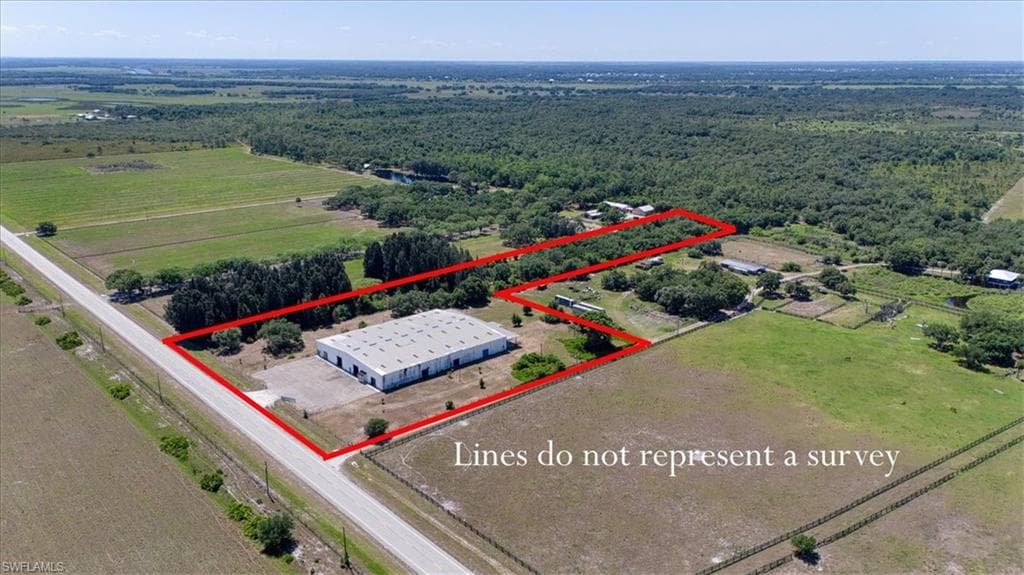 Expansive lot featuring a large commercial building with a metal roof, open fields, and mature trees