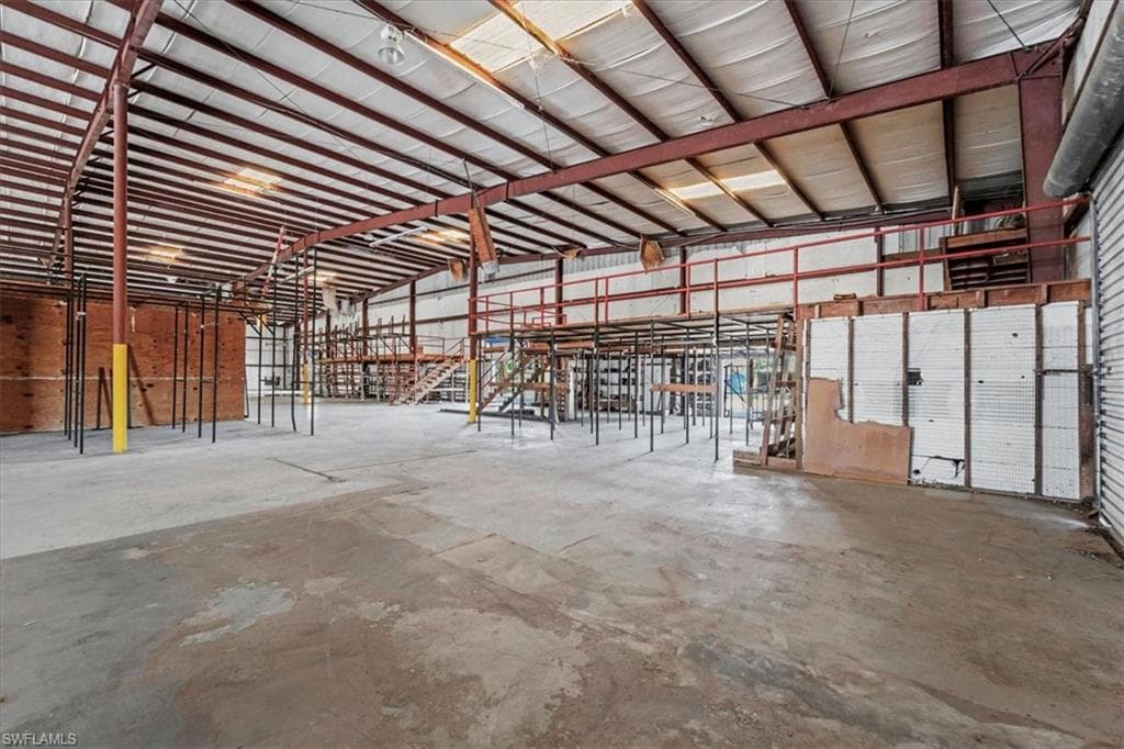 Spacious commercial interior featuring concrete flooring, exposed structural steel beams, high ceilings, and an elevated mezzanine