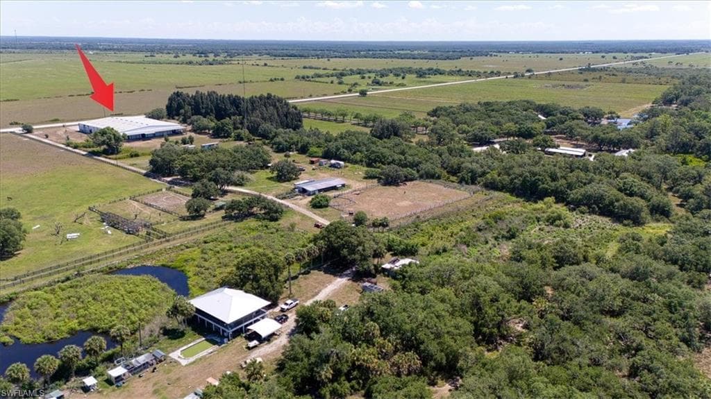Expansive rural landscape featuring a large industrial-style building with a metal roof, surrounded by green fields and mature trees