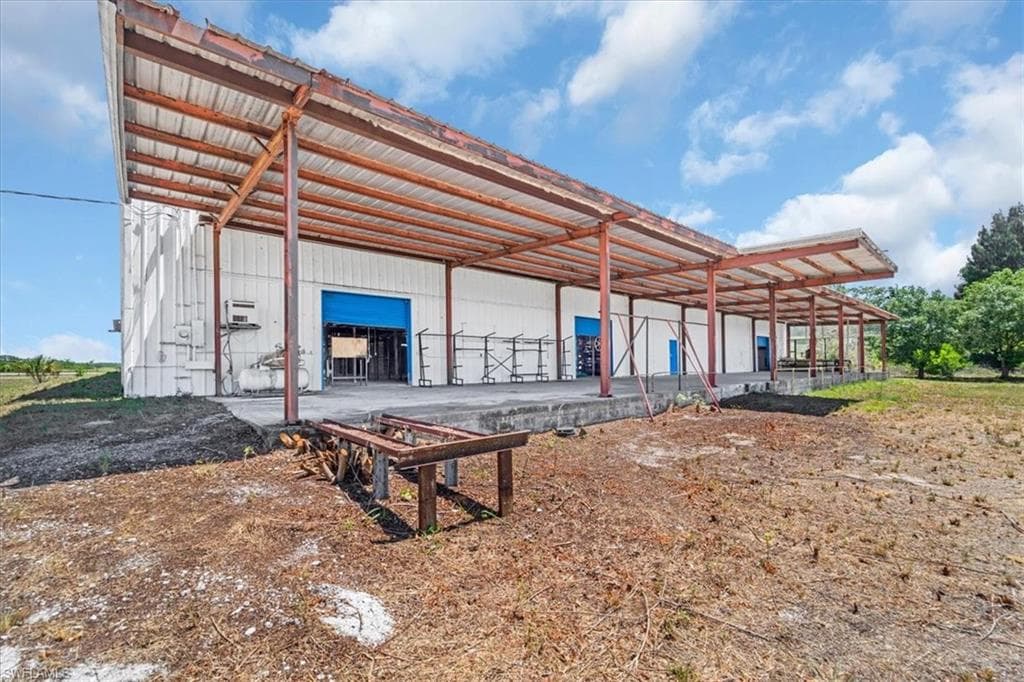 Industrial building with covered loading dock featuring multiple roll-up doors, a corrugated metal roof, and a white metal exterior
