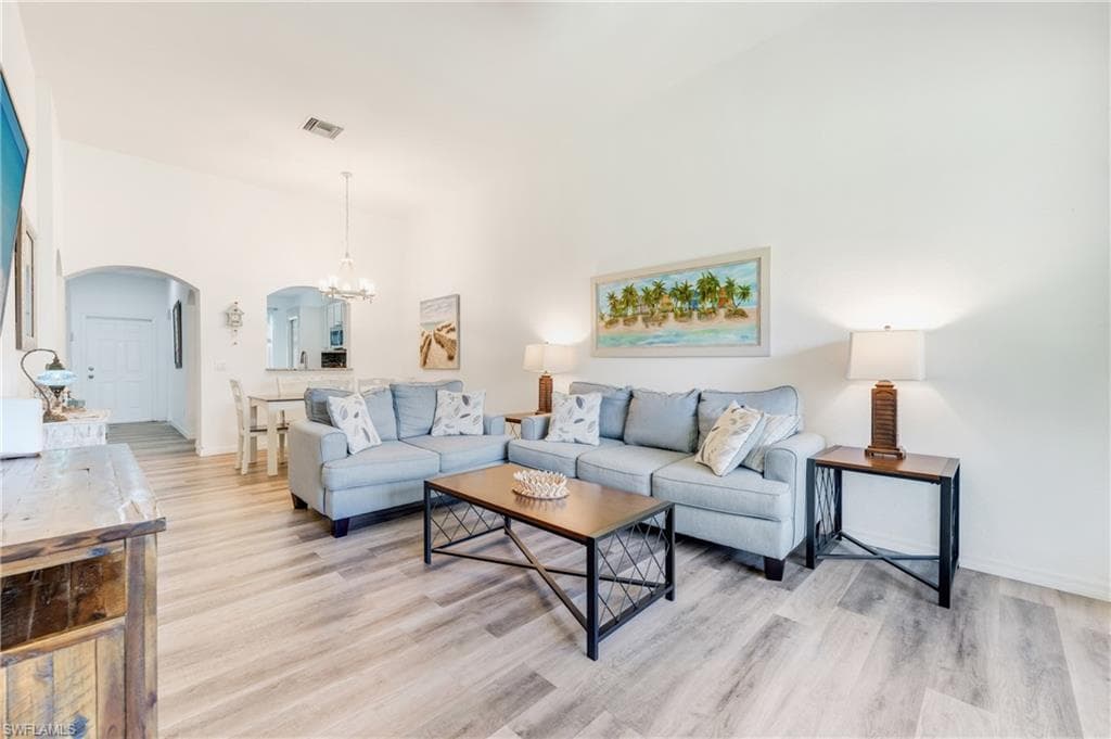 Open-concept living space featuring LVP flooring, vaulted ceilings, and an arched entryway