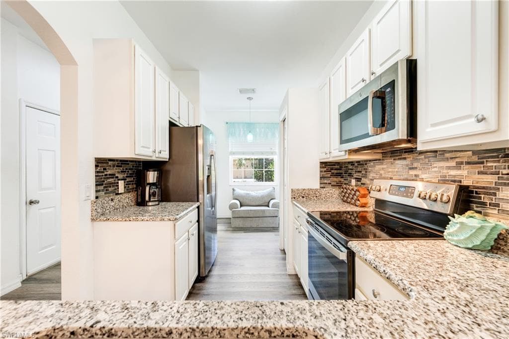 Galley kitchen featuring white cabinetry, granite countertops, stainless steel appliances, a mosaic tile backsplash, and wood-finish flooring