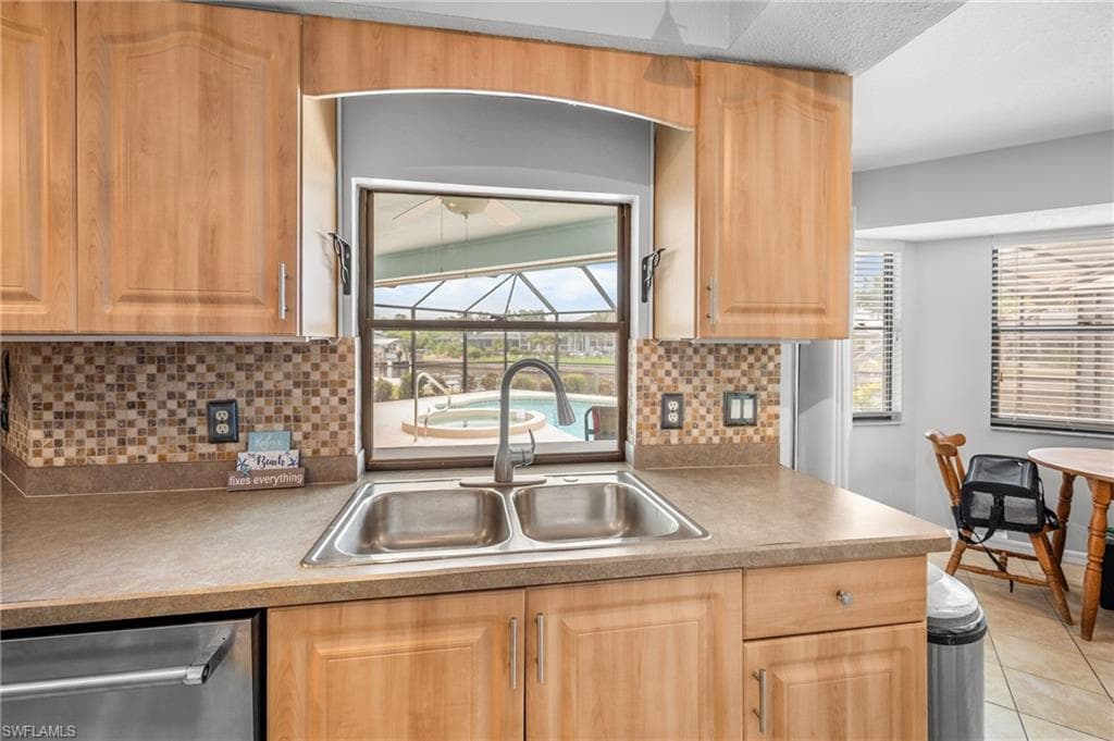 Kitchen featuring light wood cabinetry, a dual-basin stainless steel sink with a gooseneck faucet, and a mosaic tile backsplash