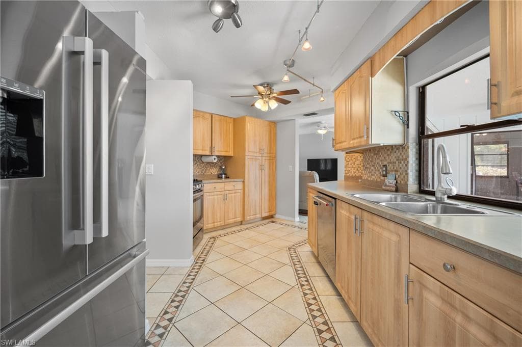 Kitchen featuring stainless steel appliances, light wood cabinetry, and a patterned tile floor