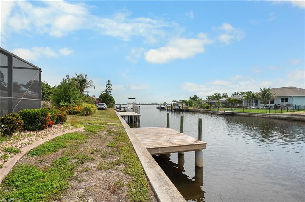 Waterfront property featuring a private wooden dock, direct canal access, a screened enclosure, mature landscaping, and a manicured lawn